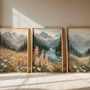 May include: Three framed landscape art prints. Each features a mountain scene with a lake or valley, wildflowers, and evergreen trees. The artwork has a vintage aesthetic with soft colors and a gold frame.