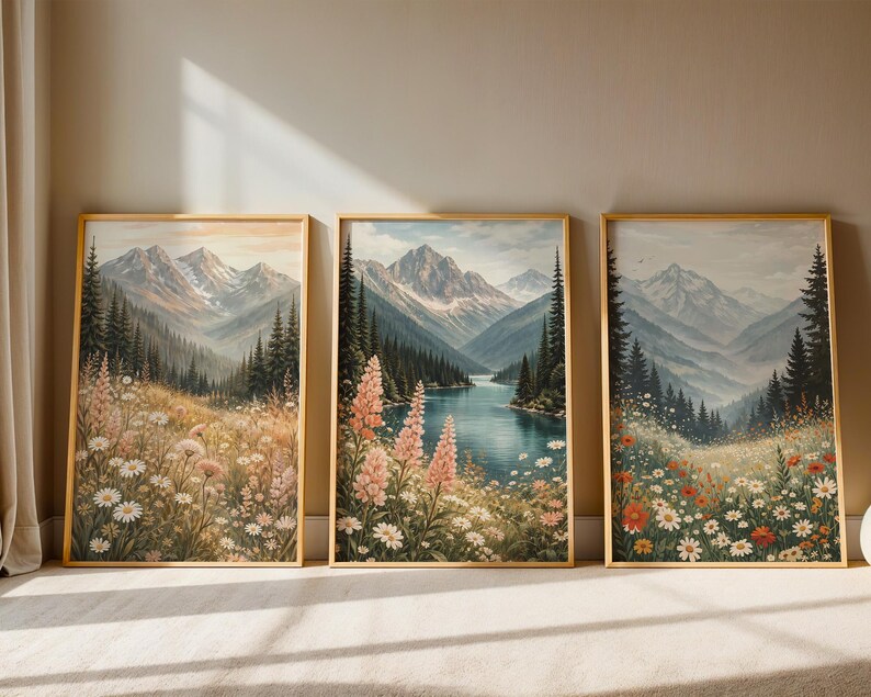 May include: Three framed landscape art prints. Each features a mountain scene with a lake or valley, wildflowers, and evergreen trees. The artwork has a vintage aesthetic with soft colors and a gold frame.