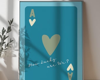 May include: A framed print with a blue background and a large green heart in the center. The text "How lucky are we?" is written in white cursive script below the heart. The ace of hearts is depicted in the top left corner and bottom right corner of the print.