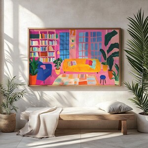 Puede incluir: Una pintura enmarcada de una sala de estar con un sof&aacute; amarillo, un sill&oacute;n azul y una estanter&iacute;a llena de libros. La habitaci&oacute;n est&aacute; pintada en tonos de rosa y cuenta con una gran ventana con vistas al exterior. La pintura est&aacute; colocada contra una pared blanca con un banco de madera en primer plano.