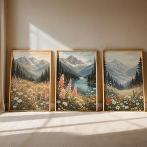 May include: Three framed landscape art prints. Each features a mountain scene with a river or lake, wildflowers, and evergreen trees. The artwork has a soft, watercolor-like quality with a warm color palette.