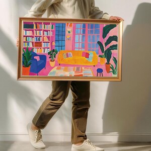 Puede incluir: Una ilustraci&oacute;n enmarcada de una sala de estar con una pared rosa, un sof&aacute; amarillo, un sill&oacute;n azul, una estanter&iacute;a y una planta en maceta. La ilustraci&oacute;n est&aacute; en un marco dorado.