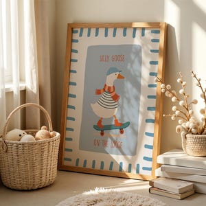 May include: A framed art print with a cartoon goose on a skateboard, wearing a hat and scarf. The print reads "SILLY GOOSE ON THE LOOSE" and has a light blue background with a light brown frame. A woven basket and decorative items are in the foreground.