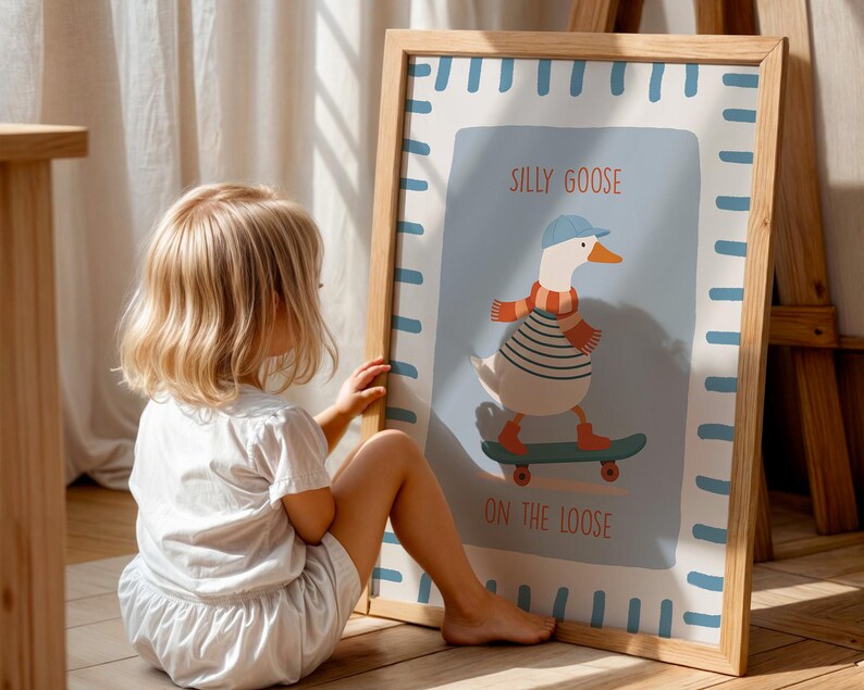 May include: A framed art print with a cartoon goose on a skateboard, wearing a blue cap and scarf. The print has a light blue background with the words "Silly Goose On The Loose" in orange text. The frame is made of light wood.