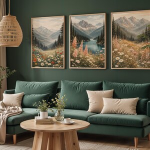 May include: Three framed landscape art prints depicting mountain scenes with wildflowers. The artwork features a color palette of greens, blues, and beige. A green velvet sofa and wooden coffee table are in the foreground.