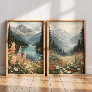 May include: Two framed landscape art prints. One features a mountain lake scene with pink flowers, the other a meadow with wildflowers. Both have wooden frames and depict mountains, trees, and water in a watercolor style.