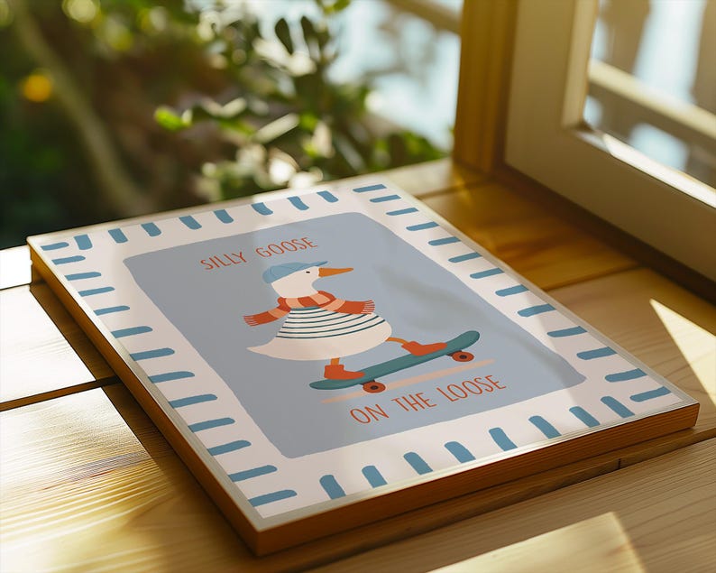 May include: A framed art print with a cartoon goose on a skateboard. The goose is wearing a blue cap, striped shirt, and scarf. The text reads "Silly Goose On The Loose" in orange. The frame has a light blue border.
