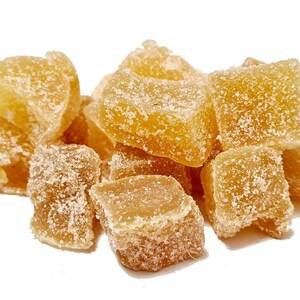 May include: A close-up of a pile of candied ginger. The ginger is a light amber colour and has a slightly grainy texture. The ginger is arranged in a random pattern.