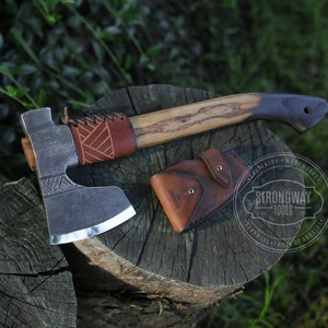 Puede incluir: Hacha con mango de madera y funda de cuero. La cabeza del hacha es de metal y tiene una hoja afilada. El mango es de color marrón claro con un agarre marrón más oscuro. La funda de cuero es marrón y tiene un cierre de botón.