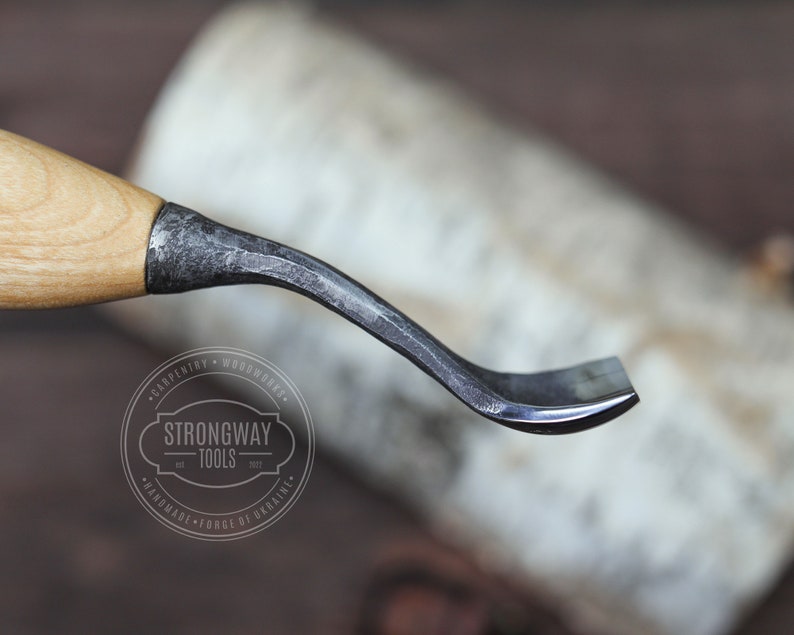 May include: A curved wood carving tool with a wooden handle and a metal blade. The blade is slightly curved and has a sharp edge. The tool is made by Strongway Tools, a company that specializes in handmade tools.