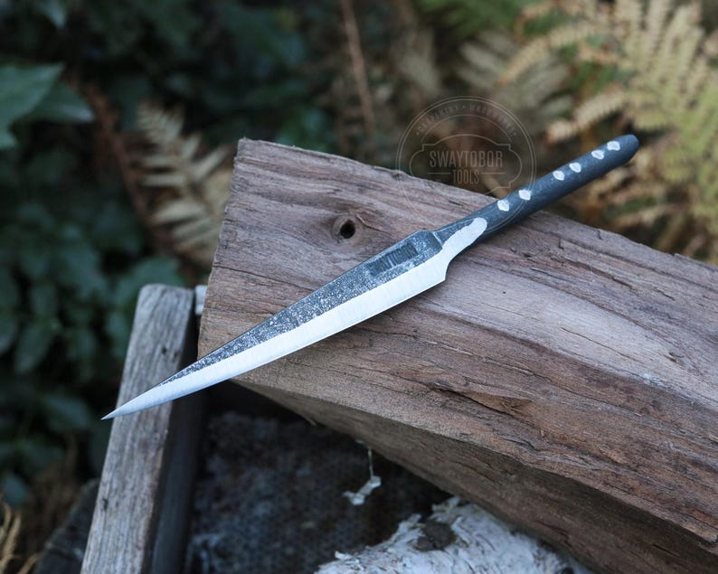 May include: A handmade knife with a silver blade and a dark gray handle with white dot accents. The knife is resting on a weathered wooden surface, showcasing its sharp design and craftsmanship. The blade is approximately 8 inches long.