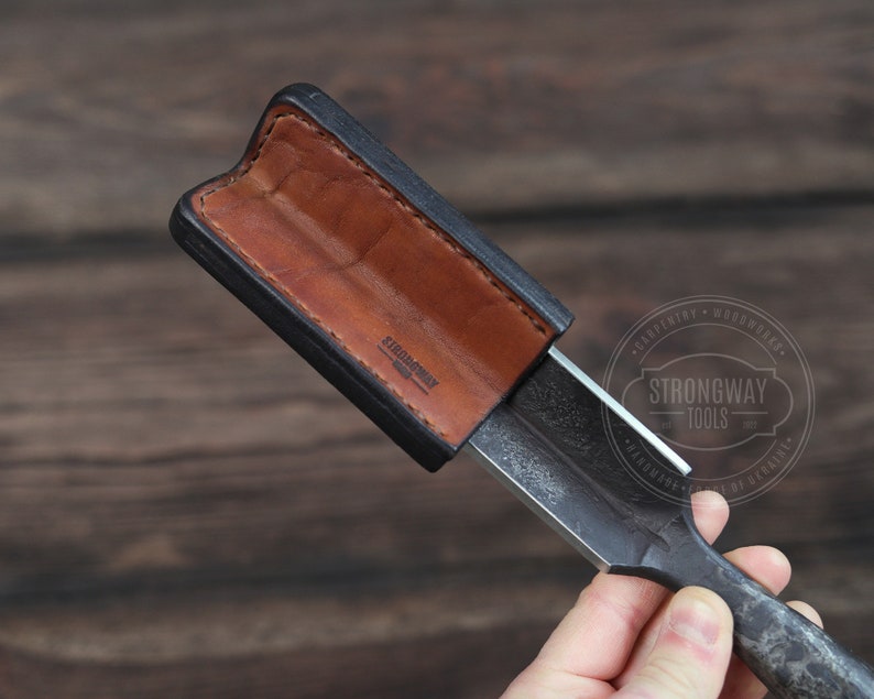 May include: A black leather sheath with a brown leather lining, holding a metal chisel with the text "Strongway Tools" on the handle.