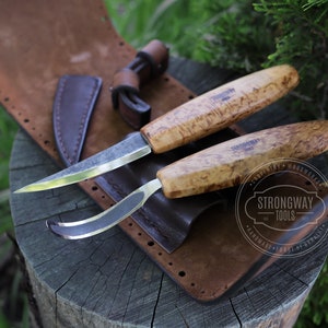 May include: Two wood carving knives with brown wood handles and a leather sheath. The knives are labeled "Strongway Tools" and "Carpentry & Woodworks".
