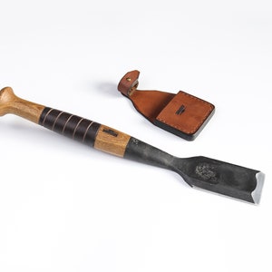 Könnte beinhalten: Ein Holzgriff-Meißel mit schwarzem Lederüberzug und einer schwarzen Metallklinge. Der Meißel wird mit einer braunen Lederscheide mit Druckknopfverschluss geliefert.