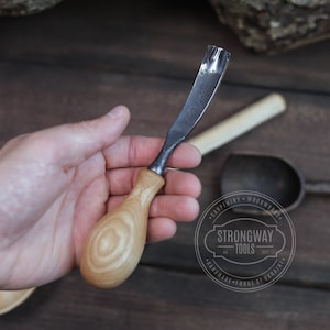 May include: A hand holds a wooden handled carving tool with a metal blade. The tool is made by Strongway Tools, a company that hand-forges tools in Ukraine.