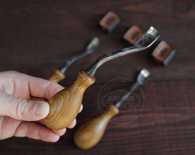 May include: Three wood carving tools with curved blades and wooden handles. The tools are on a dark wood surface. The tools are labeled "Strongway Tools".