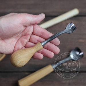 Pu&ograve; includere: Uno strumento per intagliare il legno con un manico in legno e una lama in metallo. Lo strumento &egrave; tenuto in una mano. Lo strumento &egrave; etichettato "Strongway Tools" e "Handmade - Forge of Ukraine".