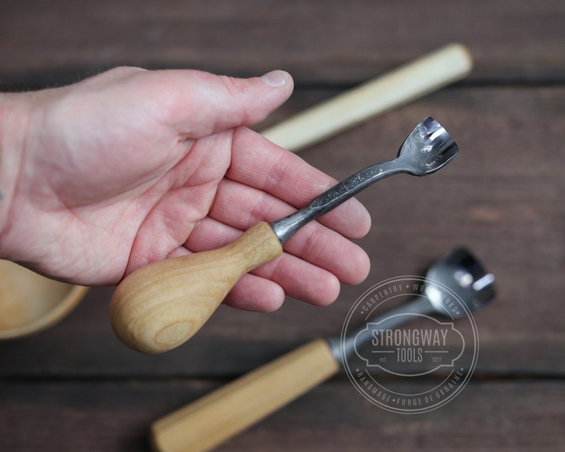 Pu&ograve; includere: Uno strumento per intagliare il legno con un manico in legno e una lama in metallo. Lo strumento &egrave; tenuto in una mano. Lo strumento &egrave; etichettato "Strongway Tools" e "Handmade - Forge of Ukraine".