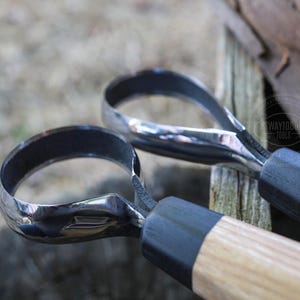 May include: Close-up of two metal carving tools with curved blades and wooden handles. The blades are shiny and reflect the light, while the handles have a natural wood grain. The tools are designed for woodworking.