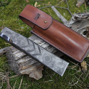 Puede incluir: Un martillo con un acabado texturizado martillado y una funda de cuero. La funda es marrón y tiene el texto "Strongway Tools" grabado en relieve.
