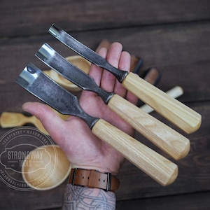 May include: Three wood carving tools with wooden handles. The tools have metal blades and are held in a hand. The tools are labeled "Strongway Tools" and "Handmade from Origin."