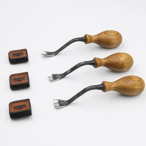 May include: Three wood carving tools with wooden handles and metal blades. The tools are on a white surface.