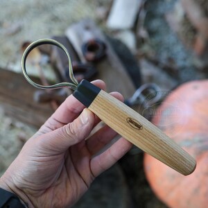 May include: A wood-handled loop tool with a black ferrule and a metal loop. The tool has the brand name "Swaydogue Tools" printed on the wooden handle. The tool is designed for shaping clay or other materials.