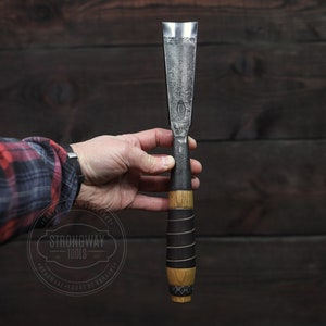 May include: A hand holds a wood-handled chisel with a black leather wrap and a metal blade. The chisel is labelled "Strongway Tools" with the text "Handmade, Forge & Crafted".