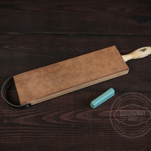 May include: A brown leather strop with a wooden handle and a metal loop. A small turquoise honing stone is also pictured. The strop is labeled "Strongway Tools".