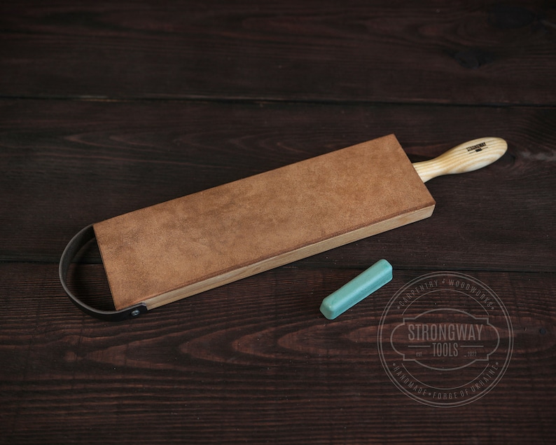 May include: A brown leather strop with a wooden handle and a metal loop. A small turquoise honing stone is also pictured. The strop is labeled "Strongway Tools".