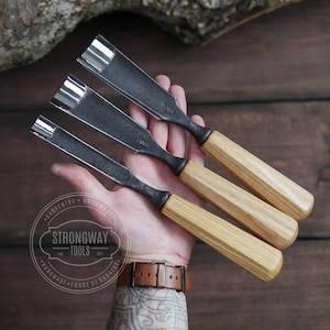May include: Three wood carving tools with curved blades and wooden handles. The tools are held in a hand with a tattoo. The tools are labeled "Strongway Tools" and "Handmade - Force of Ukraine".