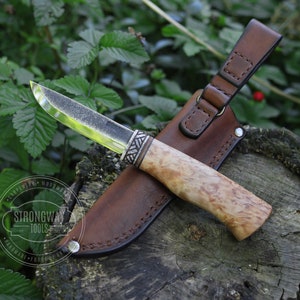 May include: A brown leather sheath with a  knife with a wood handle and a silver metal accent. The knife is partially out of the sheath. The sheath has a loop for hanging. The knife is on a wooden surface. The text "Strongway Tools" is on the sheath.