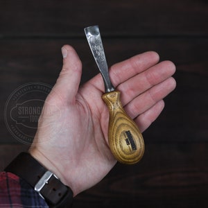 Peut inclure: Un outil de sculpture sur bois avec une poignée en bois. L'outil a une lame en métal et une poignée en bois avec une teinte brun foncé. La poignée a un petit logo rectangulaire noir avec le texte "Strongway Tools" dessus.