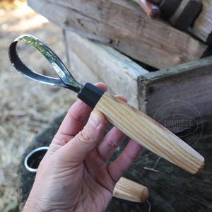 May include: A wood carving gouge with a curved, polished steel blade and a light-colored wooden handle. The handle has a black ferrule where it meets the blade. The tool is designed for woodworking and carving.