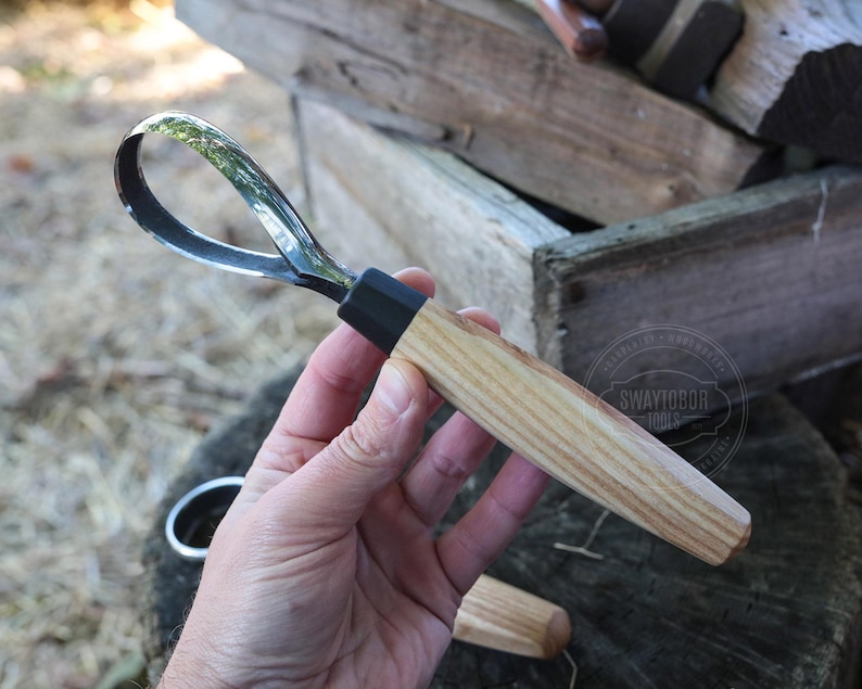 May include: A wood carving gouge with a curved, polished steel blade and a light-colored wooden handle. The handle has a black ferrule where it meets the blade. The tool is designed for woodworking and carving.