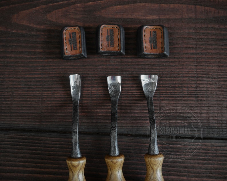 May include: Three wood carving tools with brown wooden handles and metal blades. The tools are arranged in a row on a dark brown wooden surface. The tools are labeled "Strongway Tools" in a white circle.