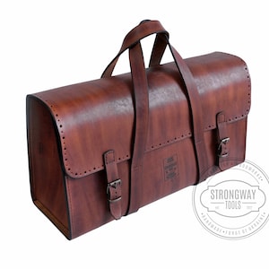 May include: A brown leather tool bag with two buckles and a handle. The bag has a label that says "Strongway Tools" and "Handmade - Forge of Ukraine".
