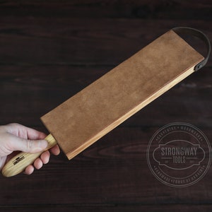 May include: A brown leather strop with a wooden handle. The strop is attached to a wooden block with a leather strap. The handle is labeled "Strongway Tools".