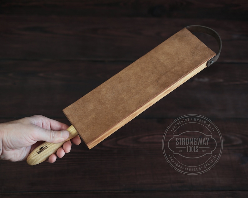 May include: A brown leather strop with a wooden handle. The strop is attached to a wooden block with a leather strap. The handle is labeled "Strongway Tools".