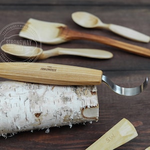Op de afbeelding: Een houtsnij-haakgereedschap met een houten handvat. Het gereedschap ligt op een stuk berkenbast. Het handvat is gegraveerd met de woorden "Strongway Tools".
