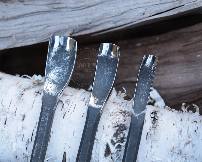 Może przedstawiać: Zbliżenie trzech metalowych narzędzi do rzeźbienia z zakrzywionymi ostrzami. Narzędzia są srebrne i mają teksturowany wygląd. Narzędzia są ułożone na kawałku kory brzozy, z drewnianym tłem. Narzędzia są oznaczone tekstem "SWAYTOBO TOOLS".