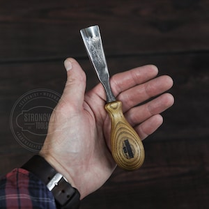 May include: A close-up of a wood carving tool with a wooden handle. The handle is engraved with the words "Strongway Tools".