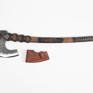 May include: A hand-forged Viking axe with a black wooden handle wrapped in leather. The axe head has a hammered finish and the handle is decorated with runes. The axe comes with a brown leather sheath.