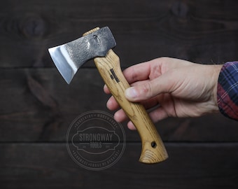 May include: A small, hand-forged axe with a wooden handle. The axe head is black with a silver blade. The handle is a light brown wood with a dark brown stain. The axe is labeled "Strongway Tools" and "Handmade Forge of Ukraine".