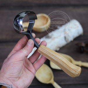 以下が含まれることがあります： 湾曲した金属製の刃と木製のハンドルが付いた木彫りの道具。道具は人の手に握られています。道具には「Strongway Tools」のラベルが付いています。