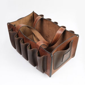 May include: A brown leather tote bag with multiple pockets and a brown leather handle. The bag is open and the interior is visible.