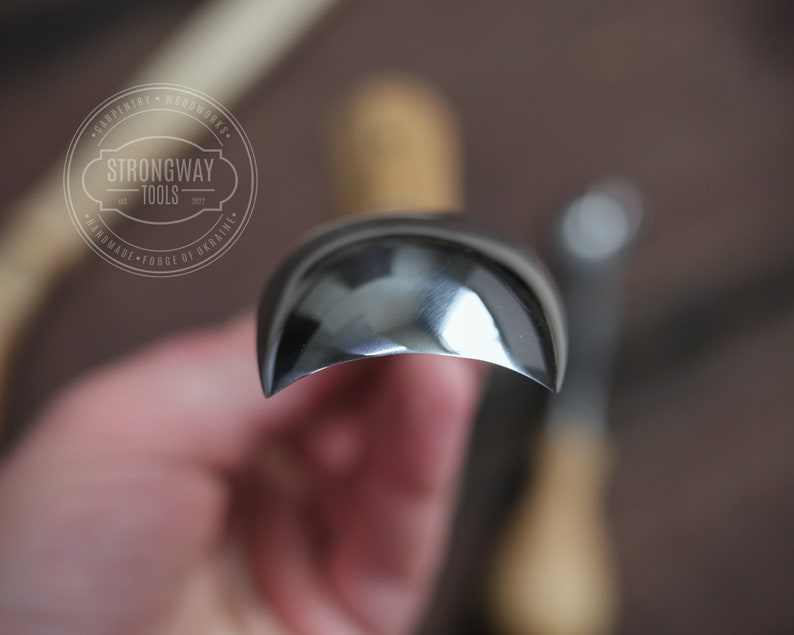 Pu&ograve; includere: Primo piano di uno strumento da intaglio in metallo curvo, lucido e color argento. Lo strumento &egrave; tenuto in una mano, con lo sfondo sfocato.