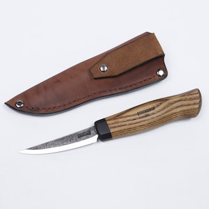 Puede incluir: Una funda de cuero marrón con un pequeño cuchillo curvo con mango de madera. El cuchillo tiene un mango negro con el texto "Strongway" en él.