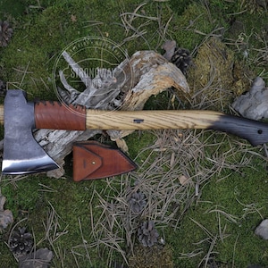 May include: A hand-forged axe with a brown leather handle wrap and a wooden handle. The axe has a black leather sheath with a brown leather strap.