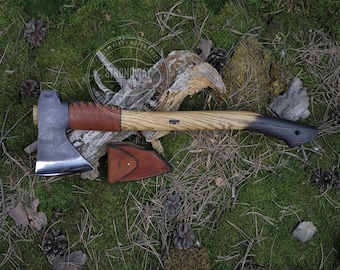 May include: A hand-forged axe with a brown leather handle wrap and a wooden handle. The axe has a black leather sheath with a brown leather strap.
